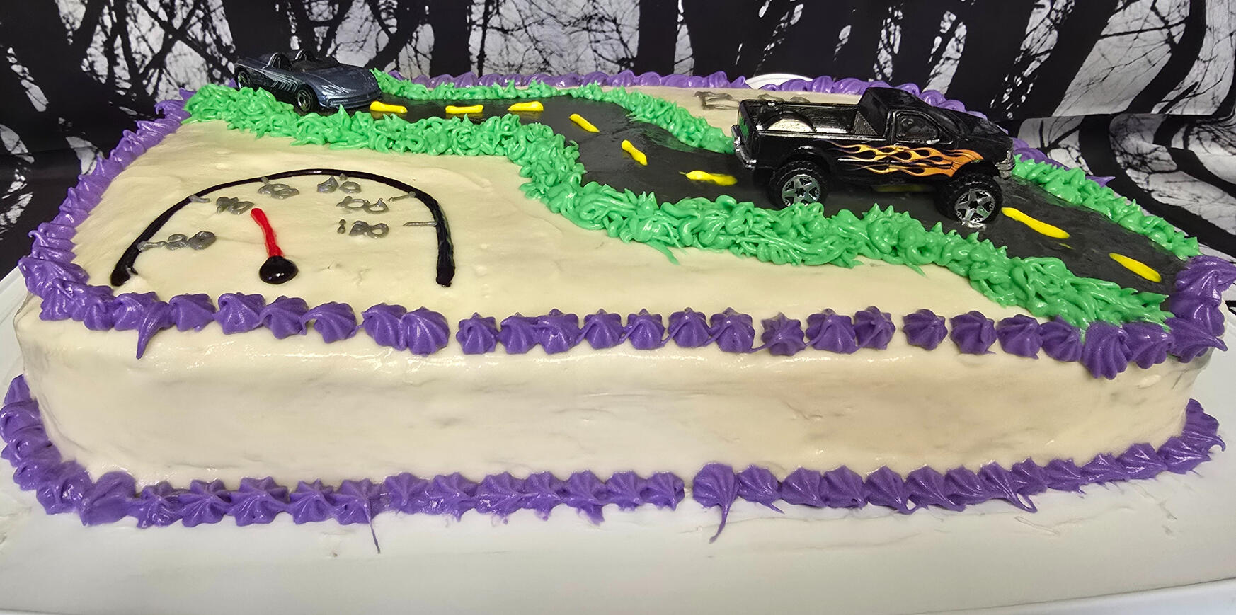 Race car sheet cake with a frosted racetrack, toy car, and speedometer design